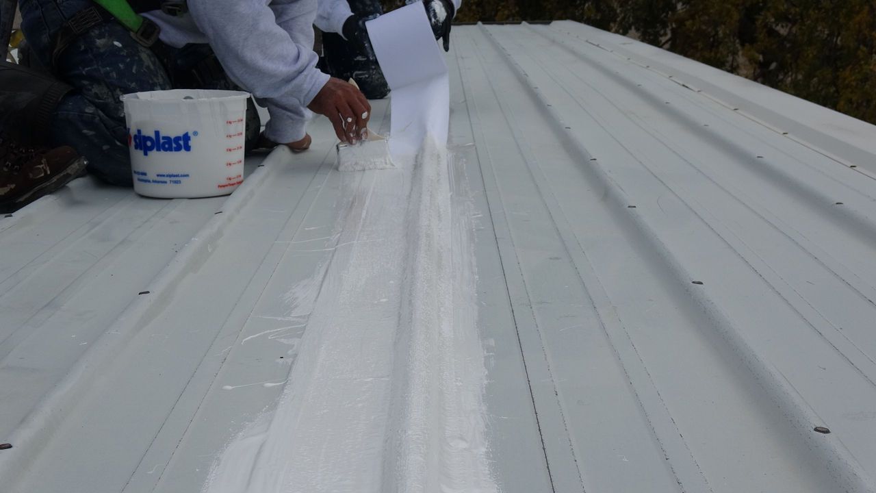 A metal roof with elastomeric roof coating being applied