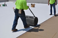 Workers applying membrane on low-slope roof.