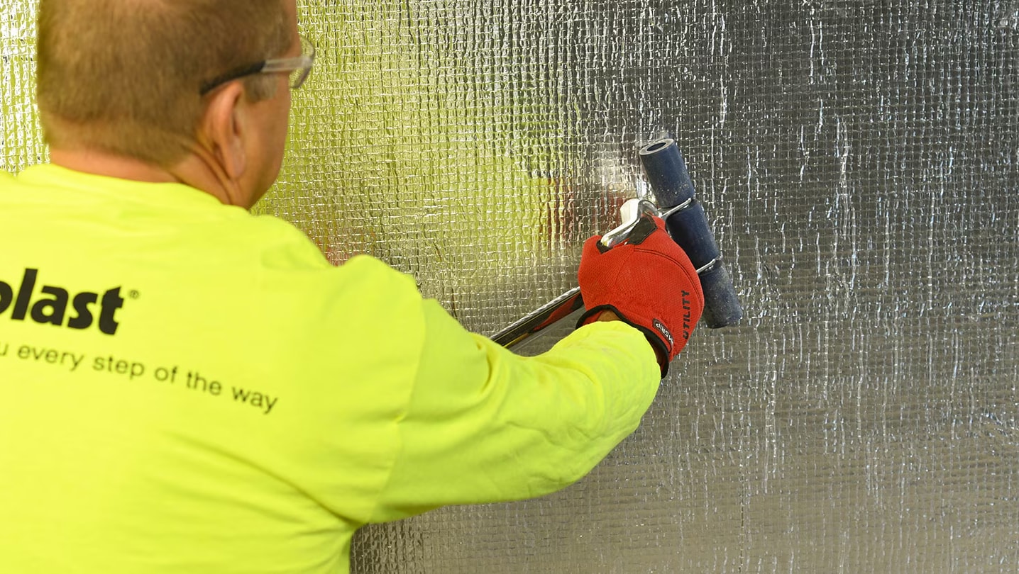 Man in siplast shirt rolling AWBs on a commercial building wall.