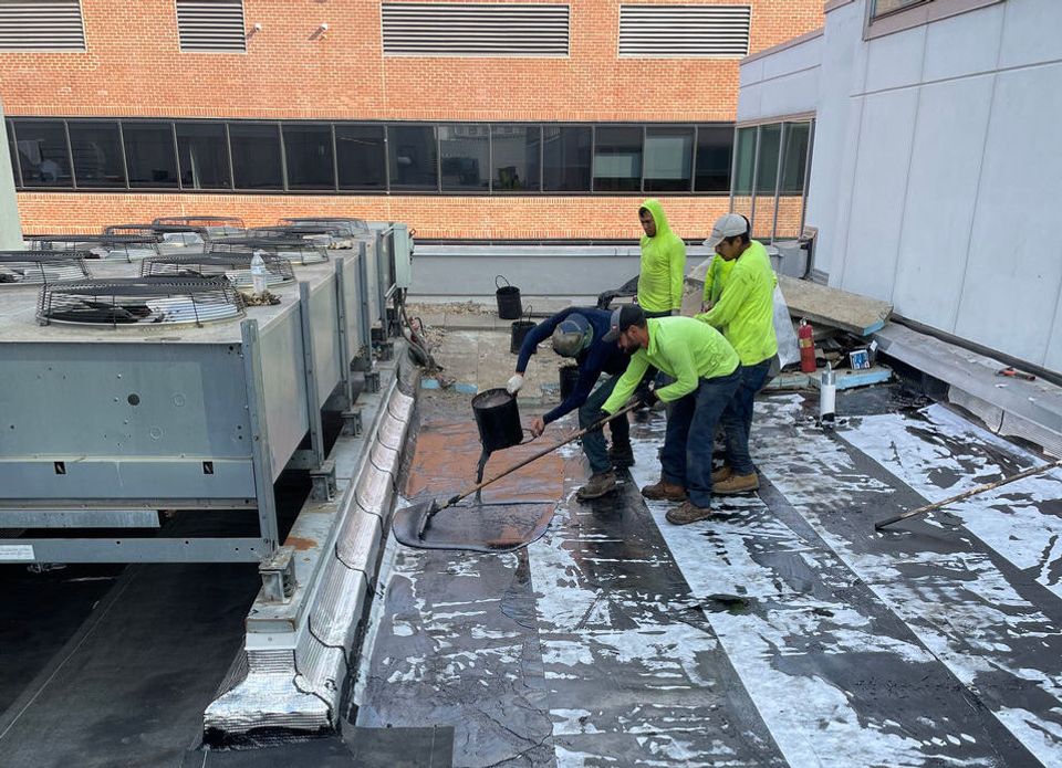 A team of roofers installing Hot-rubberized Asphalt Flashing on a commercial roof.